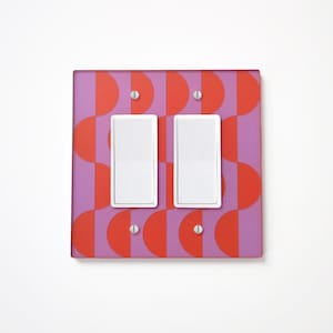Puede incluir: Una placa de cubierta para interruptor doble con un patrón geométrico de semicírculos rojos y morados.