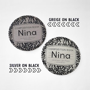 May include: Two round composition notebook coasters with a black and white speckled design. The top coaster has a grey background with black text and the bottom coaster has a silver background with black text. The text on both coasters reads "COMPOSITION BOOK" and "Nina". The top coaster has the text "130 Sheets 219 Pages Wide Ruled" and the bottom coaster has the text "100 Sheets 200 Pages Wide Ruled". The text "GREIGE ON BLACK <<<<<<<" is above the top coaster and the text "SILVER ON BLACK >>>>>>" is below the bottom coaster.