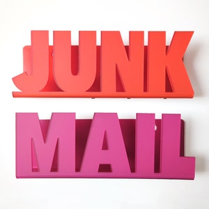 Puede incluir: Dos organizadores de correo de metal, uno rojo y otro rosa, con las palabras "JUNK" y "MAIL" recortadas en el metal.