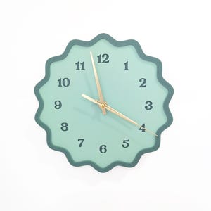 May include: A teal green clock with a wavy edge and gold hands. The clock face has black numbers 1 through 12.