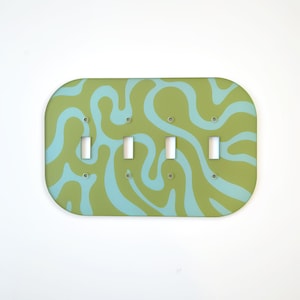 May include: A decorative light switch plate with four switches. The plate has a rounded rectangular shape and features a green and light blue swirled pattern. The switches are white.