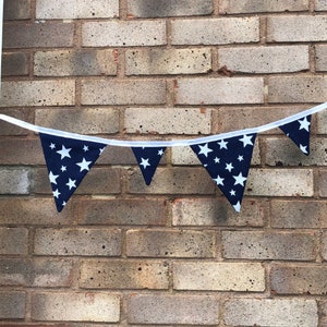 May include: A navy blue bunting with white stars, strung across a brick wall.