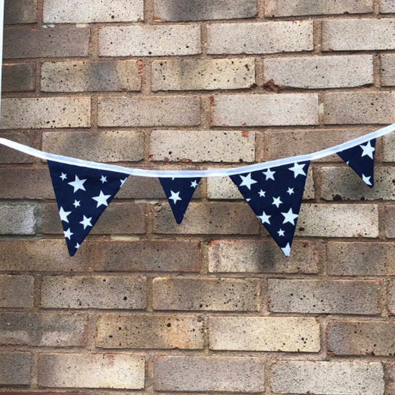 May include: A navy blue bunting with white stars, strung across a brick wall.