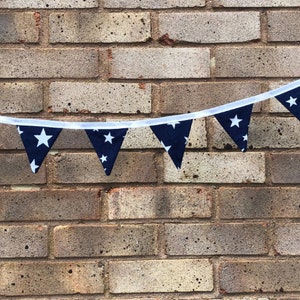 May include: A navy blue and white star patterned bunting with white string hanging against a brick wall.