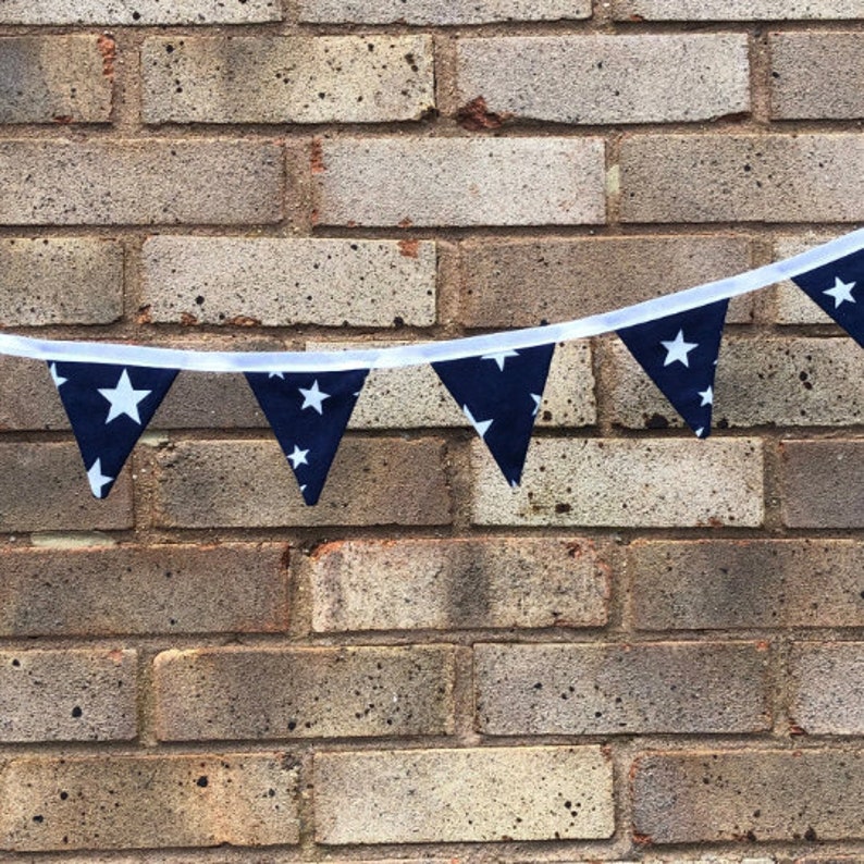May include: A navy blue and white star patterned bunting with white string hanging against a brick wall.
