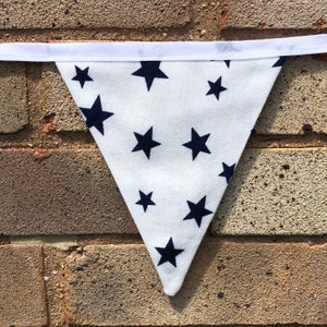 May include: White fabric bunting with a navy blue star pattern. The bunting is triangular in shape and has a white ribbon at the top.