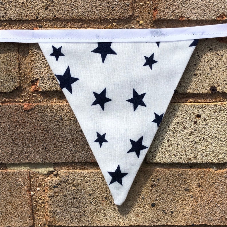 May include: White fabric bunting with a navy blue star pattern. The bunting is triangular in shape and has a white ribbon at the top.