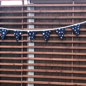 May include: A navy blue bunting with white stars hanging on a brown wooden fence.