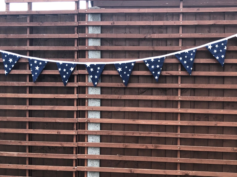 May include: A navy blue bunting with white stars hanging on a brown wooden fence.