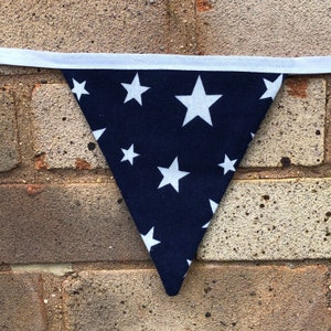 May include: A navy blue fabric pennant with white stars printed on it. The pennant is triangular in shape and has a white trim around the edges.