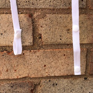 May include: Two white straps with white plastic buttons attached to a brick wall. The straps are hanging vertically.