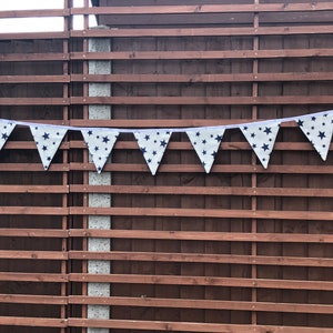 May include: A white bunting with blue stars hanging on a brown wooden fence. The bunting is made of fabric and has a white string running through it.
