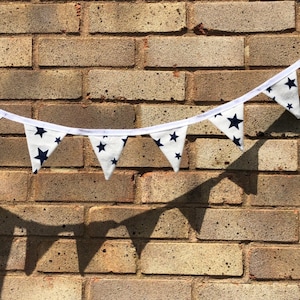 May include: A white bunting with navy blue stars hanging against a brick wall. The bunting is made of fabric and has a white string running through it.