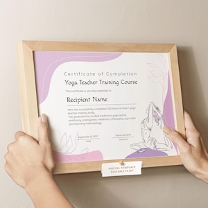 May include: A framed certificate for a Yoga Teacher Training Course. The certificate has a light purple and white design with the text "Certificate of Completion" and "Yoga Teacher Training Course". The certificate is held by two hands.