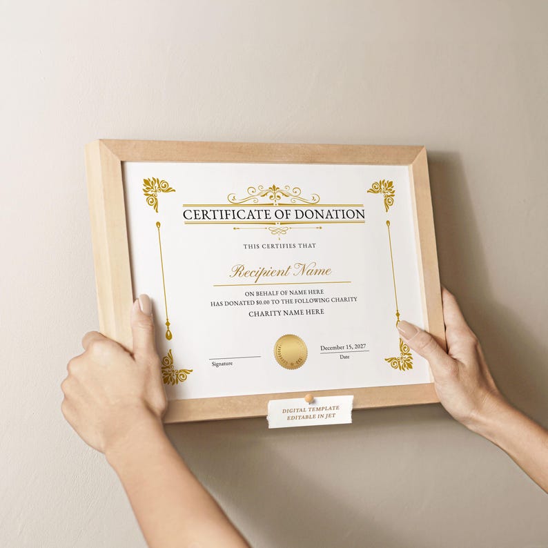 May include: A framed certificate of donation with gold accents and text. The certificate reads "Certificate of Donation" and includes fields for the recipient's name, donation amount, and charity name. The frame is light brown.