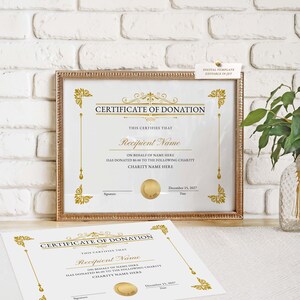 May include: A framed certificate of donation with gold accents and text. The certificate includes the words "Certificate of Donation" and "Recipient Name". A second certificate lies below the framed one.