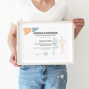May include: A framed certificate of participation for the Annual City Marathon 2027, featuring black text, abstract peach and blue shapes, and line art illustrations of two runners. The document includes placeholders for a name, signature, and date.