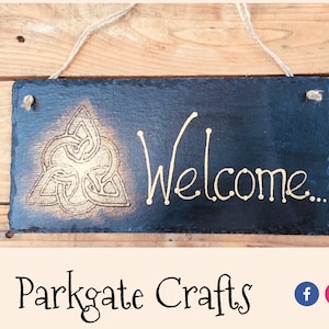 Può includere: Un cartello di benvenuto in ardesia nera con un disegno di nodo celtico dorato e la parola "Benvenuto" scritta in lettere dorate.