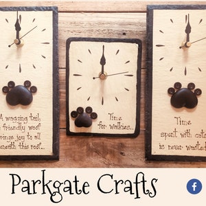 May include: Three black slate clocks with paw print designs and inspirational quotes about dogs and cats. The clocks have black hands and a cream background. The quotes are "A wagging tail, a friendly woof brings joy to all beneath this roof...", "Time for walkies...", and "Time spent with cats is never wasted..."