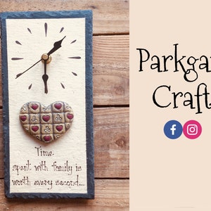 May include: A slate clock with a heart-shaped design and the text "Time spent with family is worth every second..." The clock has a black face with gold hands and a white background. The heart is made of brown and red clay with a checkered pattern.