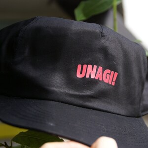 May include: Black baseball cap with a red "UNAGI!" logo.