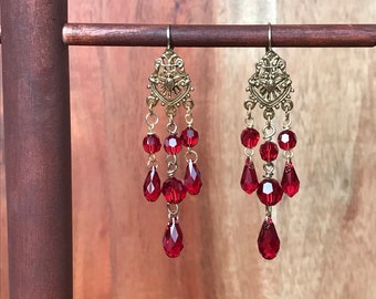 May include: A pair of gold dangle earrings with red crystal beads and teardrop-shaped drops.