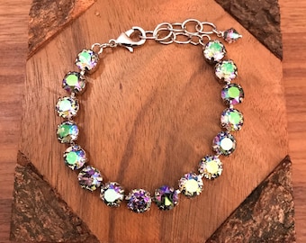 May include: A silver bracelet with iridescent green and blue crystals. The bracelet has a silver clasp and is on a wooden surface.