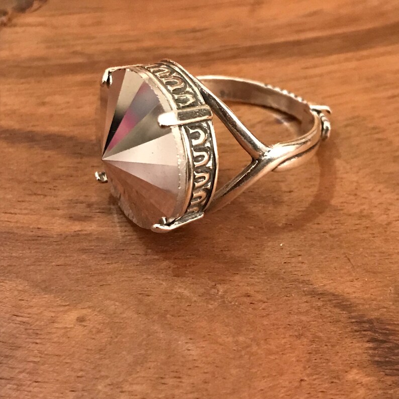 May include: A silver ring with a large, faceted, clear gemstone. The ring has a unique, twisted band design.
