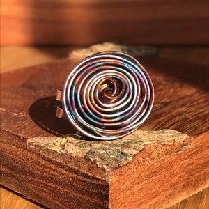 May include: A copper wire ring with a spiral design. The wire is iridescent with shades of blue, green, and purple.