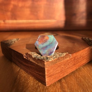 May include: A hexagonal iridescent ring with a swirling pattern of blue, green, and brown colors. The ring is sitting on a wooden surface.