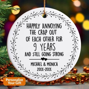 May include: White ceramic Christmas ornament with black text that reads "Happily annoying the crap out of each other for 9 years and still going strong." Includes names and dates, with a floral border.