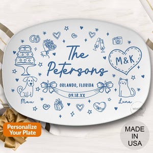 May include: White oval plate with blue line art. Features a cake, bouquet, hearts, and the text "The Petersons" with "Orlando, Florida" and a date. Includes a dog named Max and a cat named Luna. "Personalize Your Plate" text is also present.