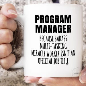 May include: A white ceramic mug featuring black printed text that reads PROGRAM MANAGER BECAUSE BADASS MULTI-TASKING MIRACLE WORKER ISN'T AN OFFICIAL JOB TITLE. The mug has a standard handle and a smooth, glossy finish with clear, bold lettering.