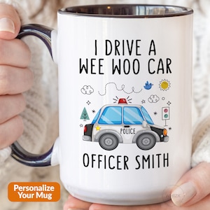 May include: White ceramic mug with a black handle. The mug features a cartoon police car with the text "I drive a wee woo car" and "Officer Smith" printed on it.