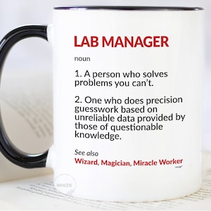 May include: White ceramic mug with a black handle and rim. The mug features the text "LAB MANAGER" in red, followed by a humorous definition. The mug also includes the words "Wizard, Magician, Miracle Worker".