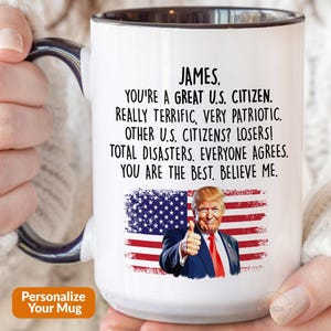 May include: A white ceramic mug with a dark blue handle and interior. The mug features a printed graphic of the American flag and a man in a suit giving a thumbs up. The text reads: James, you're a great U.S. citizen. Really terrific, very patriotic.
