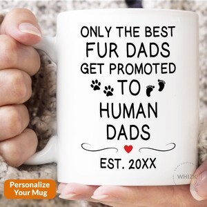 May include: White ceramic mug with the text "ONLY THE BEST FUR DADS GET PROMOTED TO HUMAN DADS" in black. The mug features paw prints, footprints, a red heart, and the text "EST. 20XX". A perfect gift for pet owners.
