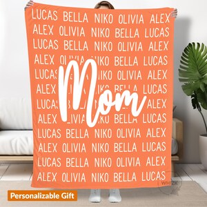 May include: A coral orange fleece blanket with the word "Mom" in white text. The blanket is personalized with a repeating pattern of names, including Lucas, Bella, Niko, Olivia, and Alex.