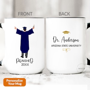 May include: White ceramic mug with a black handle. The front of the mug features a cartoon illustration of a person in a blue graduation gown with a cap and diploma. The text "FINISHED 20XX" is below the illustration. The back of the mug features the text "Dr. Anderson ARIZONA STATE UNIVERSITY" with a gold graduation cap and diploma.
