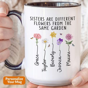 May include: White ceramic mug with a black handle and black rim. The mug has a floral design with the text "Sisters are different flowers from the same garden."  The names "Grace", "Taylor", "Beverly", "Jessica", and "Maxine" are written vertically below the flowers.