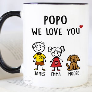 May include: White ceramic mug with a black handle. The mug has the words "POPO WE LOVE YOU" printed on it in black. There is a small red heart next to the text. Below the text are three stick figures, a boy, a girl, and a dog. The boy is wearing a yellow shirt and brown shorts. The girl is wearing a red dress. The dog is brown. The names "JAMES", "EMMA", and "MOOSE" are printed below the figures.