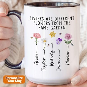 May include: White ceramic mug with a black handle and rim, featuring the text "Sisters are different flowers from the same garden." The mug displays colorful flower illustrations with names: Grace, Taylor, Beverly, Jessica, and Maxine. Butterflies are also present.