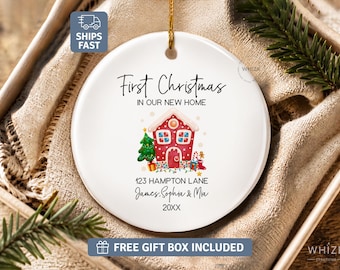 Peut inclure: Une décoration ronde en céramique blanche ornée d'une illustration de maison en pain d'épices, d'un sapin de Noël vert et de lumières colorées. Le texte indique : First Christmas IN OUR NEW HOME, 123 HAMPTON LANE, James, Sophia & Mia, 20XX.
