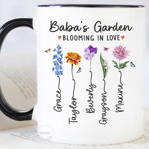 May include: White ceramic mug with a black handle and rim, featuring the text "Baba's Garden BLOOMING IN LOVE." The mug is decorated with colorful flowers and butterflies, with names below each flower.