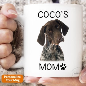 May include: White ceramic mug with a black and white image of a German Shorthaired Pointer dog. The text "Coco's Mom" is printed on the mug with a paw print.