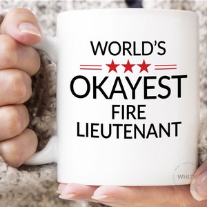 May include: White ceramic mug with black text that reads "WORLD'S  ***  OKAYEST FIRE LIEUTENANT".