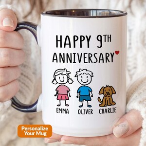 May include: A white ceramic mug with a dark blue handle and interior. The front features the black text HAPPY 9TH ANNIVERSARY with a small red heart. Below are three stick figures: a girl named Emma, a boy named Oliver, and a brown dog named Charlie.