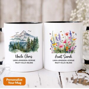 May include: Two white ceramic mugs with black handles and black rims. One mug features a watercolor illustration of a mountain range with the text "Uncle Chris" and names below. The other mug features a watercolor illustration of wildflowers with the text "Aunt Sarah" and names below.