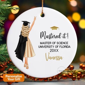May include: White ceramic graduation ornament with a blonde illustration wearing a graduation gown. Text reads "Mastered it!" and includes "Master of Science, University of Florida, 20XX, Vanessa."