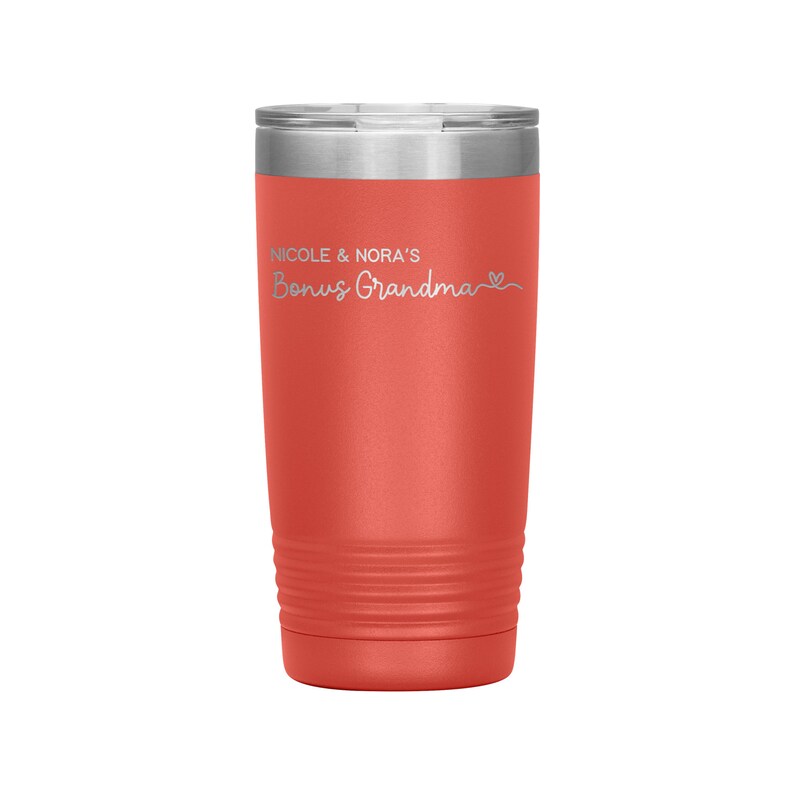 May include: Coral red stainless steel tumbler with a silver lid. The tumbler has a white inscription that reads "Nicole & Nora's Bonus Grandma" with a small heart symbol.